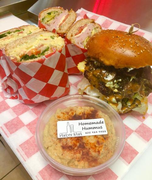 A plate featuring a sandwich, a wrap, and a container of homemade hummus with a checkered paper background.