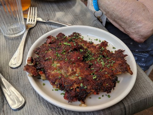 A crispy, golden-brown potato dish topped with chopped green onions, served on a white plate.