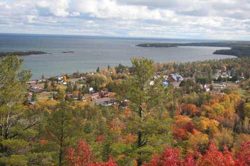 A scenic view of a colorful autumn landscape with a lake, trees, and a small town nestled along the shore.