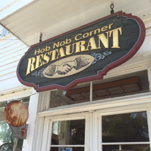 Sign for "Hob Nob Corner Restaurant" featuring a handshake graphic, hanging above a window.