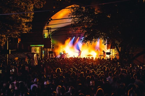A vibrant concert scene with a large crowd silhouetted against colorful stage lights and smoke.
