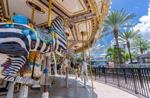 A colorful carousel featuring zebra and horse figures, surrounded by palm trees and a bright blue sky.