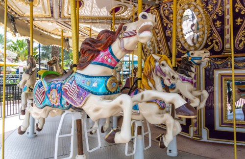 Colorful carousel horses with intricate designs, set against a vibrant, ornate backdrop.