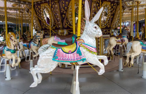 A colorful carousel featuring a white rabbit and several horses, all intricately designed and ready for riders.