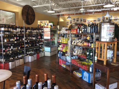 A well-stocked wine shop featuring shelves of wine bottles, snacks, and various grocery items in a bright, inviting space.