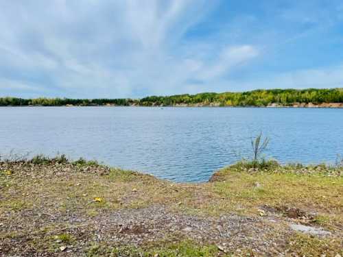 A serene lake surrounded by greenery under a blue sky with wispy clouds.