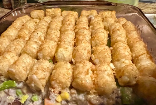 A close-up of a casserole dish topped with golden-brown tater tots, resting on a creamy vegetable filling.