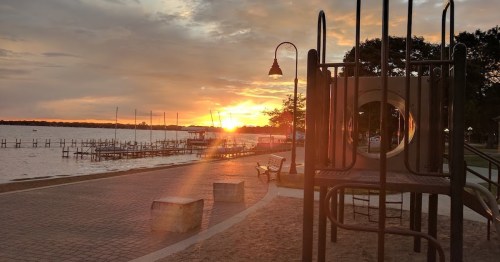 Sunset over a lake with a playground in the foreground and docks in the background, creating a serene atmosphere.