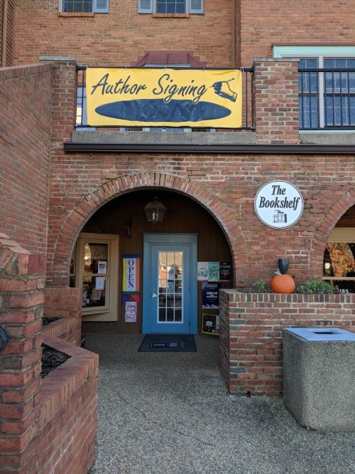 A brick building with an "Author Signing" banner above the entrance to a bookstore called "The Bookshelf."