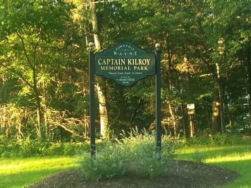 Sign for Captain Kilroy Memorial Park, surrounded by trees and greenery, indicating park hours and location.