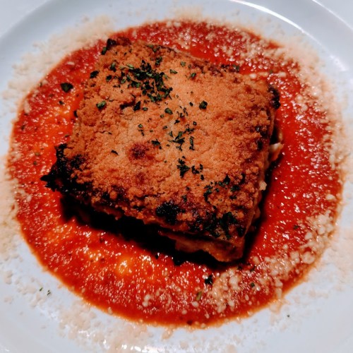 A square piece of lasagna topped with a golden crust, served on a bed of rich red tomato sauce.