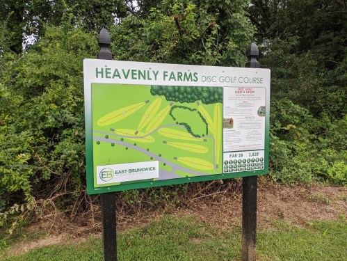 Sign for Heavenly Farms Disc Golf Course, featuring a course map and safety rules, surrounded by greenery.