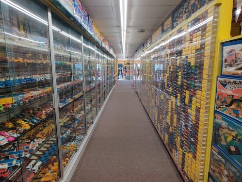 A long aisle lined with glass display cases filled with toy cars and collectibles, brightly lit and colorful.