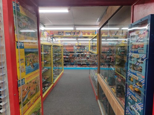 A colorful toy store aisle lined with glass display cases filled with various model cars and collectibles.