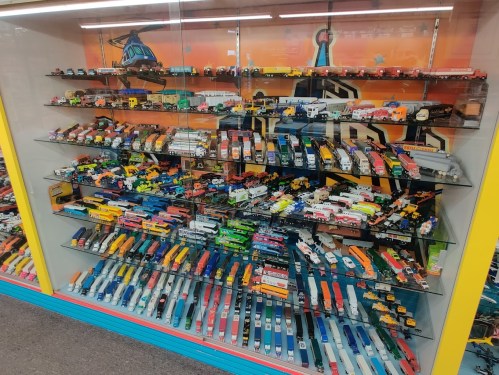A display case filled with colorful toy trains, trucks, and vehicles arranged on multiple shelves.
