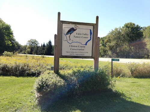 Sign for Eden Valley Nature Center, featuring a heron illustration and surrounded by greenery and wildflowers.