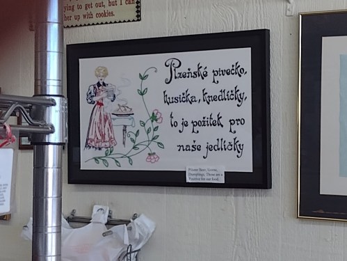 A framed sign with a vintage illustration and text about traditional Czech food, featuring a woman cooking.
