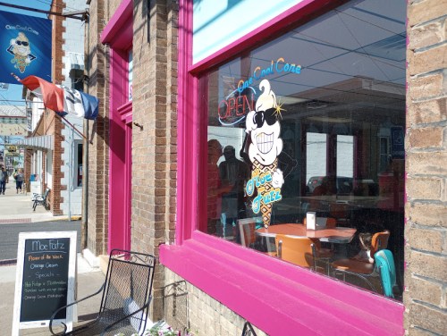 A colorful ice cream shop with a cartoon ice cream cone in the window, featuring outdoor seating and a "Open" sign.