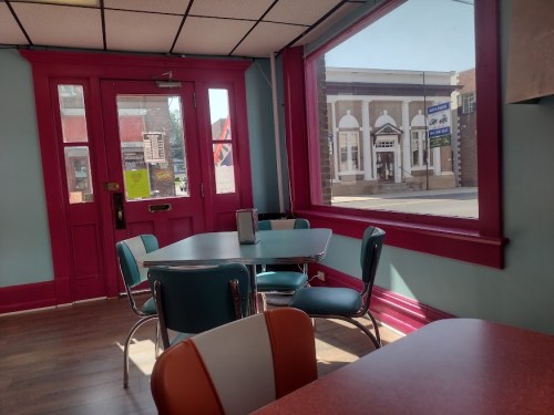 A cozy diner interior with teal and red decor, featuring tables and a large window overlooking a street.