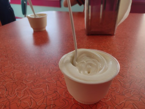 A small cup of soft-serve ice cream with a spoon, placed on a vibrant orange table.