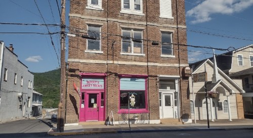A brick building with a pink storefront labeled "Tammy's Sweet Meats" and nearby shops on a sunny day.