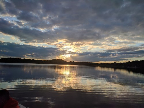A serene lake at sunset, with clouds reflecting on the water and a warm glow in the sky.