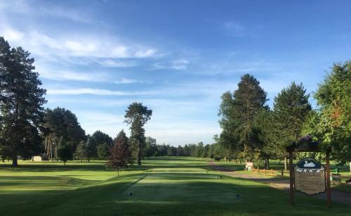 A scenic view of a golf course with lush green grass, trees, and a clear blue sky. A sign for SLGC is visible.
