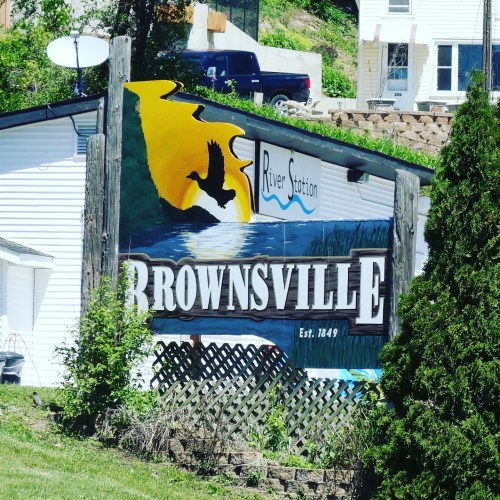 Sign for Brownsville, featuring a scenic mural with a bird and sunset, alongside "River Station" and establishment year 1849.