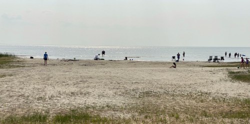 A sandy beach with people walking along the shore and enjoying the water on a sunny day.