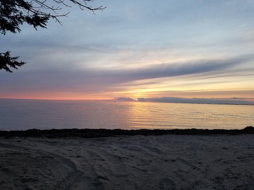 A serene beach at sunset, with colorful skies reflecting on calm waters and a sandy shore in the foreground.