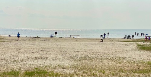 A sandy beach with people walking, playing, and relaxing near the water under a bright sky.