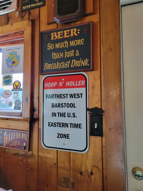 Sign on a wooden wall reads: "Hoop N' Holler, Farthest West Barstool in the U.S. Eastern Time Zone."