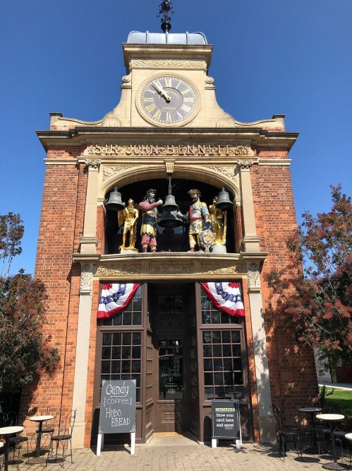 Historic brick building with a clock, featuring statues and patriotic decorations, and a sign for candy and groceries.