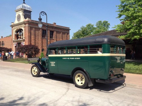 A vintage green and black bus parked on a street near a historic building with people in the background.