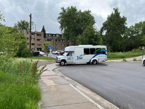 A white shuttle bus with "Via" branding turns at a street corner near a residential building and greenery.