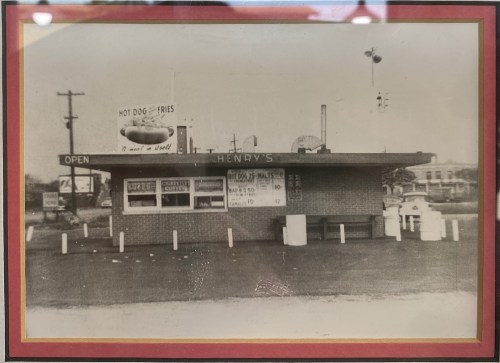 Black and white photo of a vintage fast food stand named "Henry's," featuring a menu for hot dogs and fries.