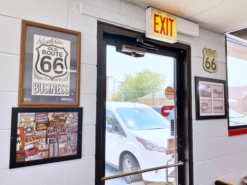 Interior view of a diner featuring Route 66 decor, an exit sign, and a glimpse of a car outside.