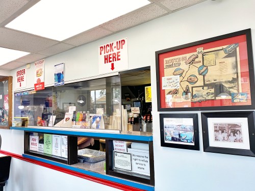 A restaurant counter with signs for ordering and pick-up, featuring Route 66 memorabilia on the wall.