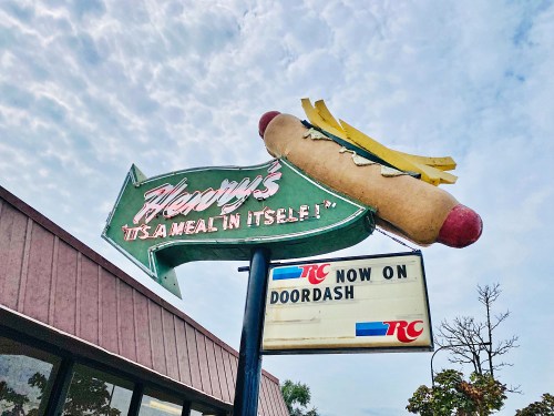 A vintage sign for a hot dog restaurant featuring a large hot dog and the text "Now on DoorDash."