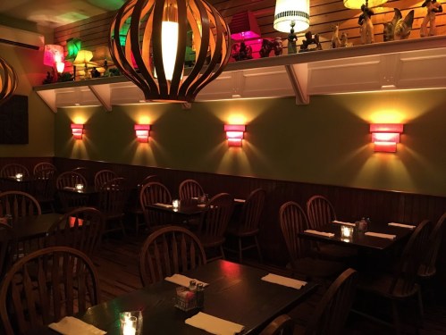 Cozy restaurant interior with wooden tables, chairs, and colorful lamps illuminating the walls. Warm, inviting atmosphere.