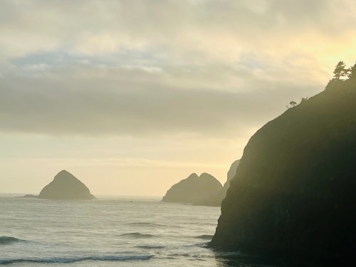 A serene coastal scene with misty cliffs and distant rock formations under a soft, cloudy sky.