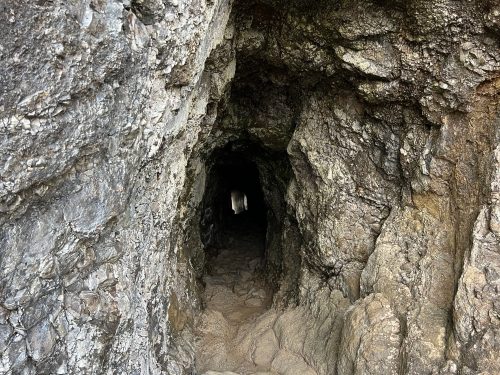 A narrow cave entrance with rocky walls, leading into a dark tunnel.