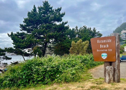 Sign for Oceanside Beach Recreation Site surrounded by greenery and trees, with a cloudy sky in the background.