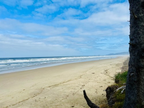 A serene beach scene with gentle waves, sandy shore, and a cloudy blue sky in the background.