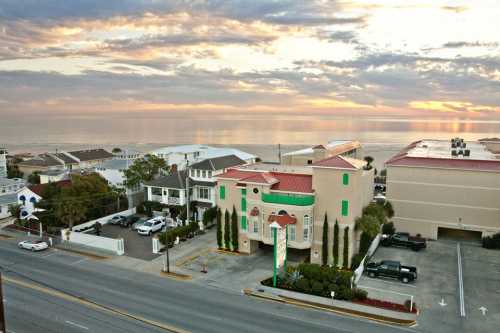 A coastal view at sunset featuring a colorful building, ocean, and a quiet street lined with parked cars.