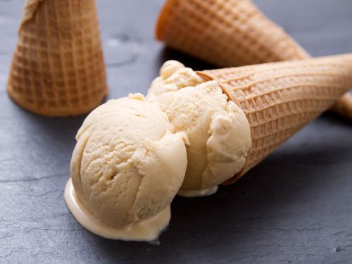 Two ice cream cones, one tipped over with a scoop of vanilla ice cream melting onto a dark slate surface.