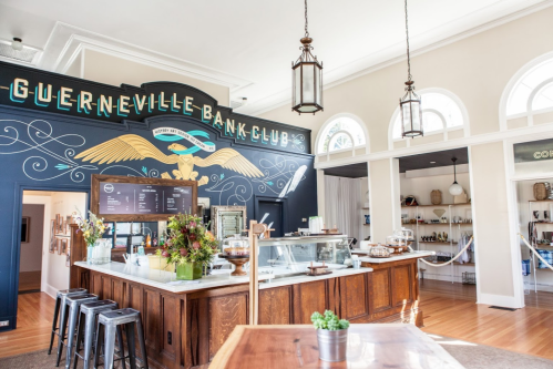 Interior of the Guerneville Bank Club, featuring a stylish counter, decorative wall art, and bright, airy atmosphere.