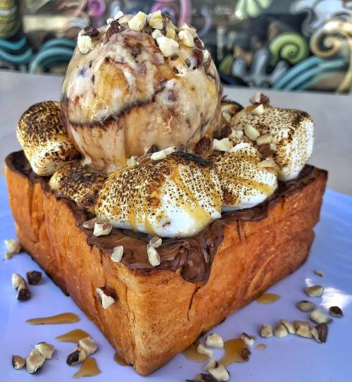 A thick slice of toasted bread topped with chocolate spread, toasted marshmallows, nuts, and a scoop of ice cream.