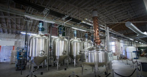 Industrial brewing facility with large stainless steel fermentation tanks and copper distillation equipment.