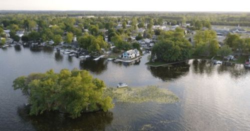 Aerial view of a serene lake with lush greenery, small boats, and a nearby town in the background.